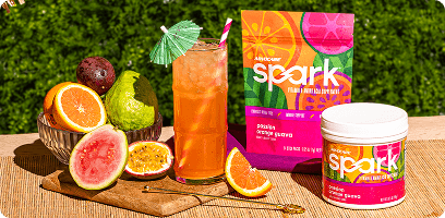 Spark Passion Orange Guava Canister & Gusset Bag sitting next to a mixed Spark POG drink along with Oranges, Passion Fruit and Guavas in a tropical environment.