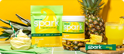 Spark Pineapple Whip Gusset Bag and Canister sitting on a green cloth surrounded by pineapples and whip ice cream against a yellow background.
