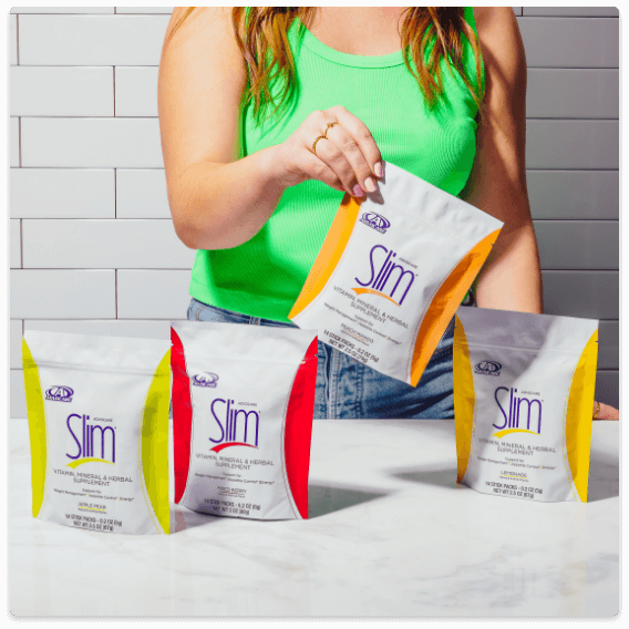 A woman with 4 gusset bags of Slim on a table in front of her. She holds one of the gusset bags up in front of her.