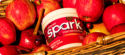 Spark Cranberry Apple Spice canister sitting in a basket of apples.