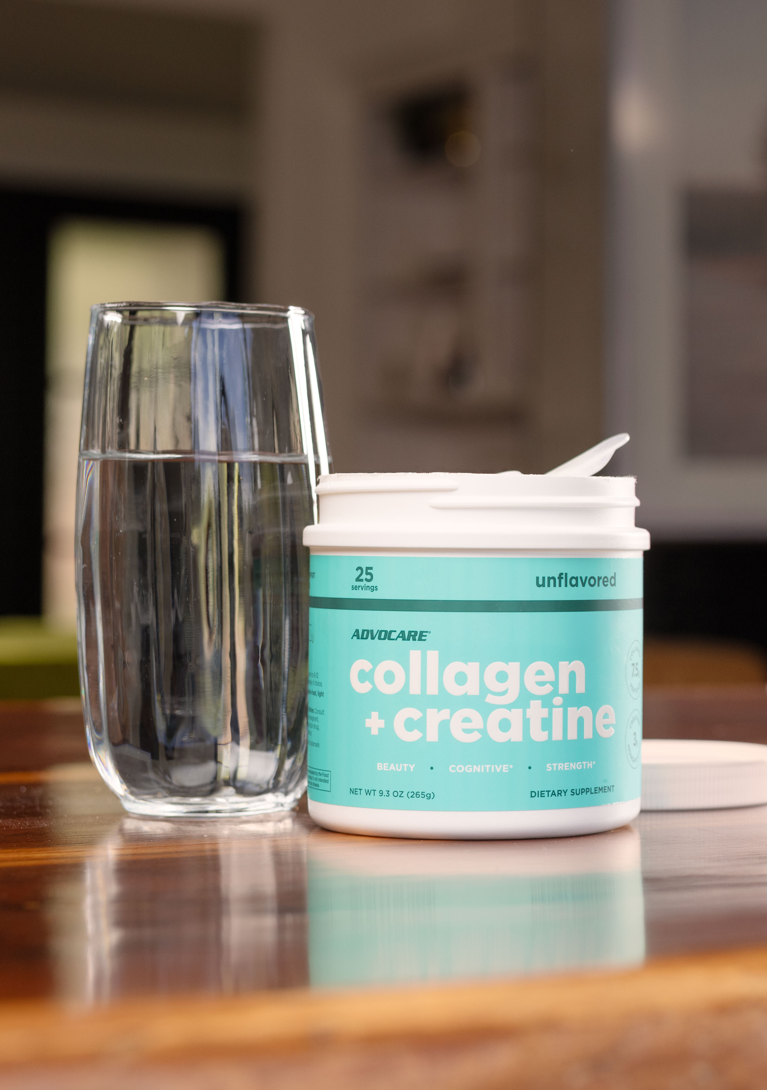 A canister of Collagen + Creatine on a table next to a glass of water.