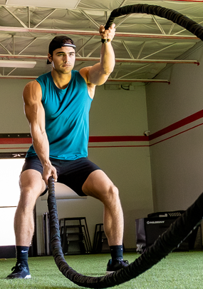 An athletic man doing exercise ropes workout in the gym.