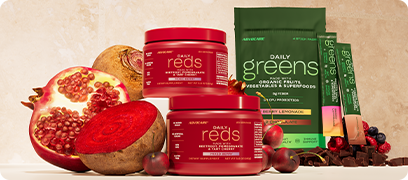 AdvoCare Daily Reds canister surrounded by sliced pomegranates and beet roots next to the Daily Greens Sample Pack.
