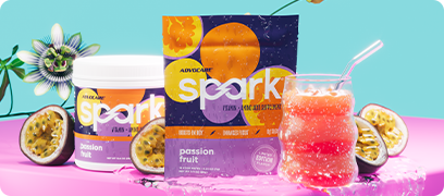 AdvoCare Spark&reg; Passion Fruit canister and stick pack surrounded by sliced passionfruit and a mixed drink in a glass container.