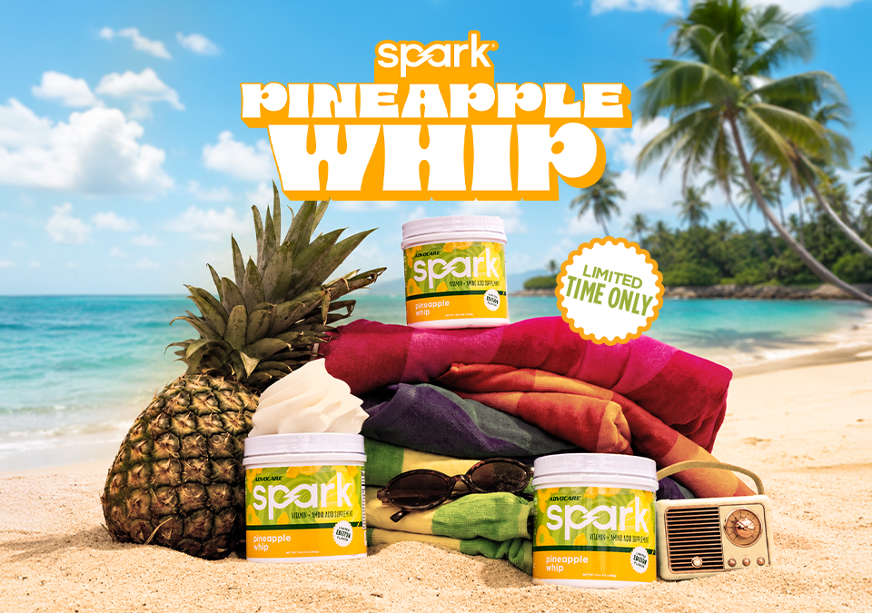 Spark Pineapple Whip canisters on a beach setting sitting on beach towels next to a pineapple.